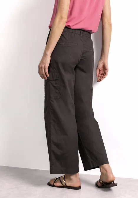 Vue de dos d'une personne portant un pantalon ample sombre, un haut rose et des sandales marron.