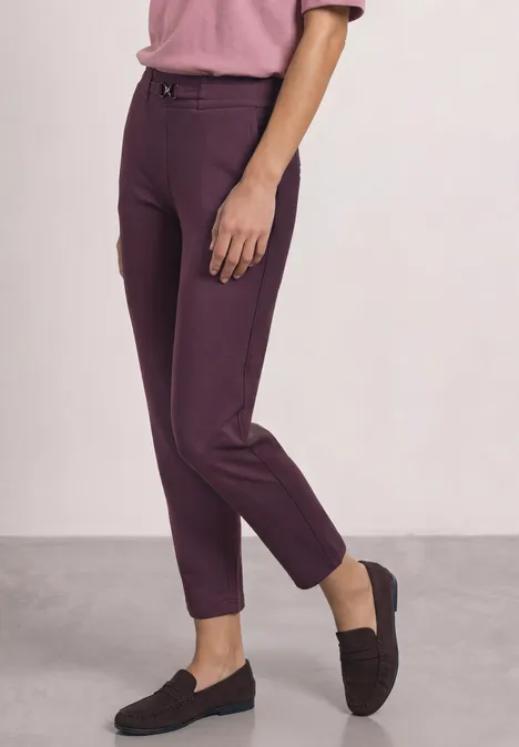 Een persoon draagt een strakke paarse broek en zwarte loafers.