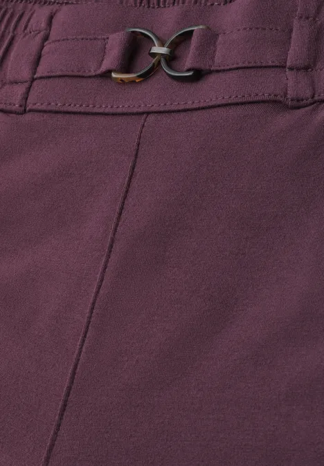 Close-up van een paars kledingstuk met siernaad en goudkleurige gesp.