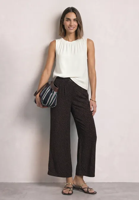 Mid Waist Straight Leg Hose mit Print molten earth Frau in weißem, ärmellosem Top und schwarzen, gepunkteten, weiten Hosen mit Sandalen und einer Umhängetasche.