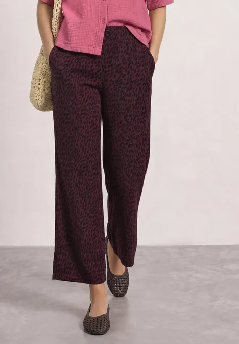 Mid Waist Straight Leg Hose mit Print rustic rouge Frau trägt weite, dunkel gemusterte Hose, rosa Bluse, schwarze Ballerinas und Strohtasche.