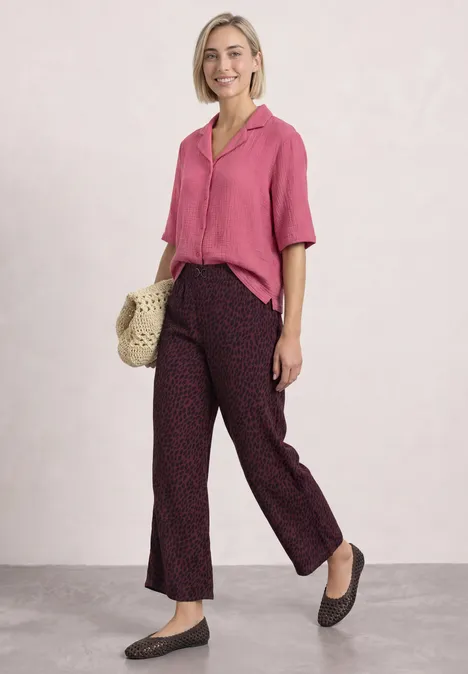 Mid Waist Straight Leg Hose mit Print rustic rouge Eine Frau trägt eine pinke Bluse, weite gepunktete Hose, Korbtasche und schwarze Ballerinas vor hellem Hintergrund