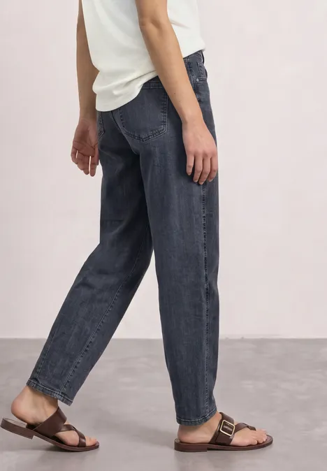 High Waist Barrel Leg Jeans im Loose Fit Steel Grey Washed Eine Person trägt dunkle, lockere Jeans und braune Sandalen, seitliche Ansicht.