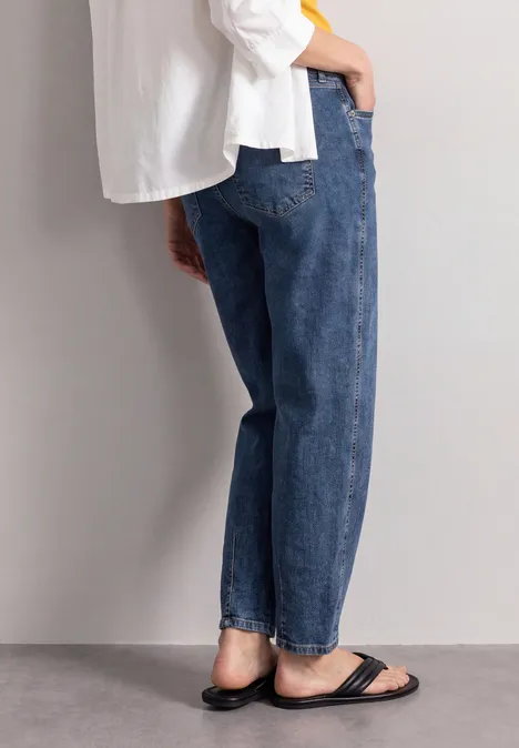 High Waist Barrel Leg Jeans im Loose Fit Medium Blue Washed Seitliche Ansicht einer Person mit weiten blauen Jeans, weißem Oberteil und schwarzen Sandalen.