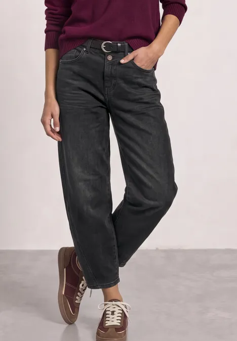 High Waist Barrel Leg Jeans im Loose Fit Black Washed Frau trägt burgunderfarbenen Pullover, schwarze, weit geschnittene Jeans und passende Sneaker.