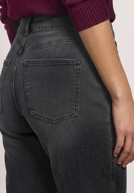 High Waist Barrel Leg Jeans im Loose Fit Black Washed Rückansicht einer Person in engen, schwarzen Jeans mit zurückgeklappten Taschen und weinrotem Pulli.