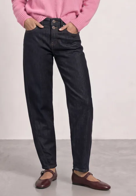 Frau trägt hochgeschnittene dunkelblaue Jeans, hellrosa Pullover und braune Ballerinas.