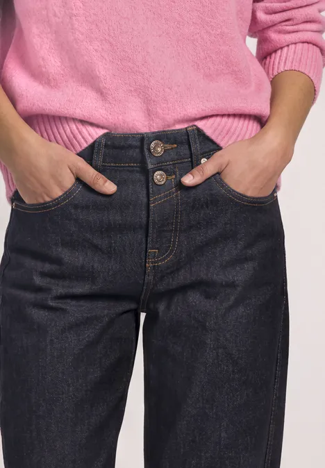 Frau in rosa Pullover und hoch sitzender dunkelblauer Jeans mit drei Knöpfen.