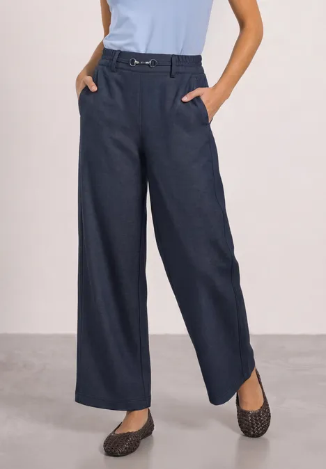 Vrouw draagt donkerblauwe wijde broek met riem, lichtblauwe top en gemêleerde instappers.