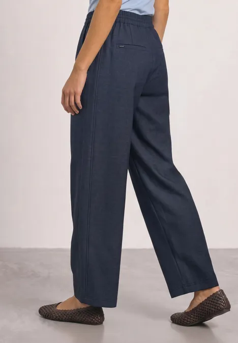 Zijaanzicht van iemand met wijde donkerblauwe broek en gestructureerde zwarte loafers.
