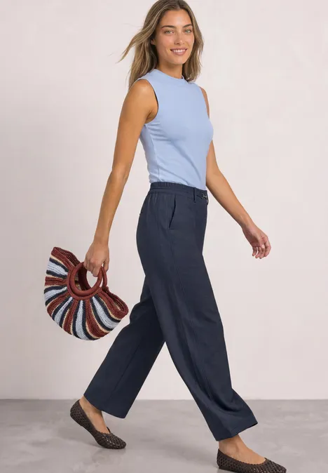 Een vrouw met lichtblauw topje en donkerblau wijde broek met gestreepte tas.