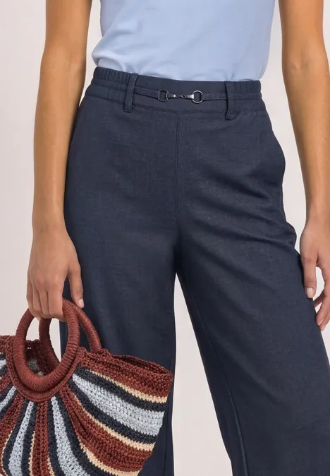 Vrouw in lichtblauw topje, donkerblauwe broek en kleurrijke rieten tas