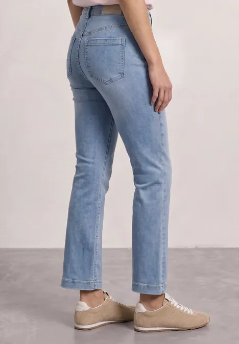 Seitlich fotografierte Frau in hellblauen, knöchellangen Jeans und beigen Sneakern.