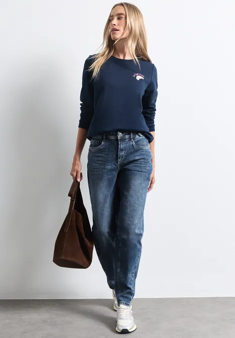Jeans met High Waist en wijd uitlopende pijpen in een Loose Fit-pasvorm Medium Blue Random Washed Vrouw in donkerblauw longsleeve, losse jeans, witte sneakers en bruine leren tas.