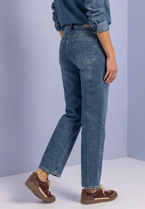 Jeans z prostymi nogawkami i guzikowymi detalami Medium Blue Random Washed Tylny widok osoby w niebieskich dżinsach i brązowych butach na jednolitym tle.