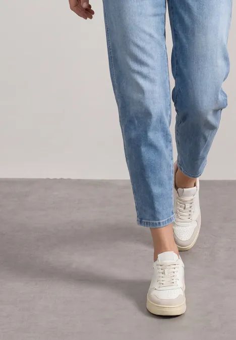 Eine Person trägt hellblaue Jeans und weiße Plateau-Sneaker und geht auf grauem Boden.