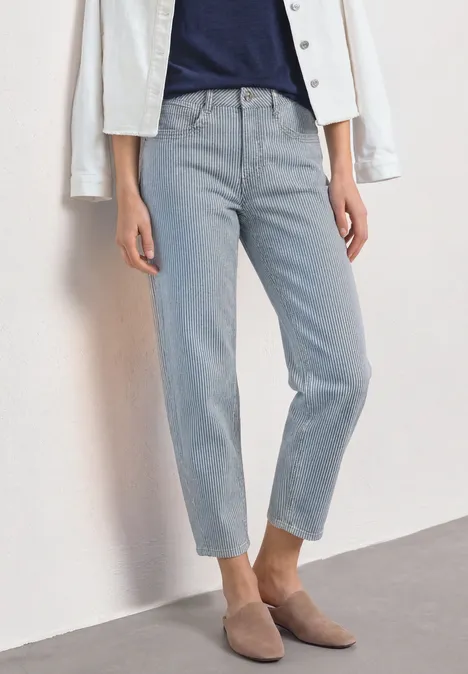 Lichte rechte jeans, donkerblauw T-shirt, witte jas en beige puntige schoenen.