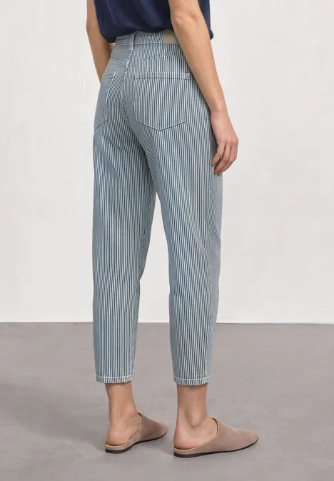 Achteraanzicht van een persoon in lichtblauwe, high-waist jeans en beige pantoffels.