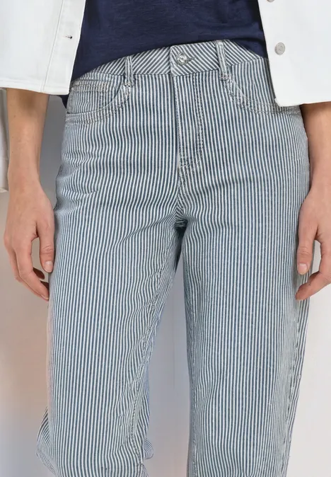 Persoon draagt een hoog getailleerde blauw-wit gestreepte jeans, gecombineerd met een donkerblauwe top en een witte jas.
