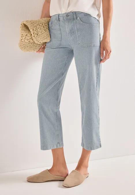 Een persoon draagt lichtblauwe, enkellange jeans, beige instappers en heeft een strozak bij zich.