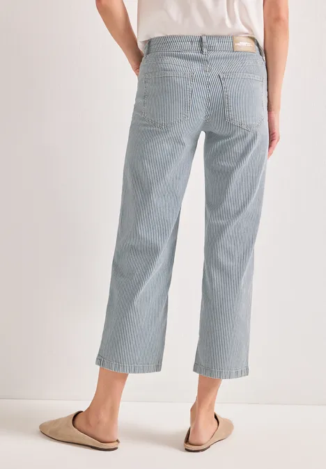 Achteraanzicht van persoon in lichtblauwe, wijde, enkellange jeans en sloffen.