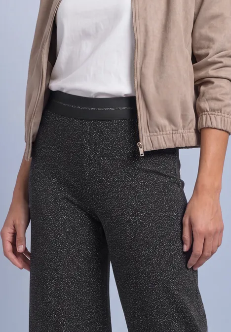 Pantalon taille haute à jambes larges avec un motif raffiné Black Personne en veste beige, t-shirt blanc et legging sombre pailleté.
