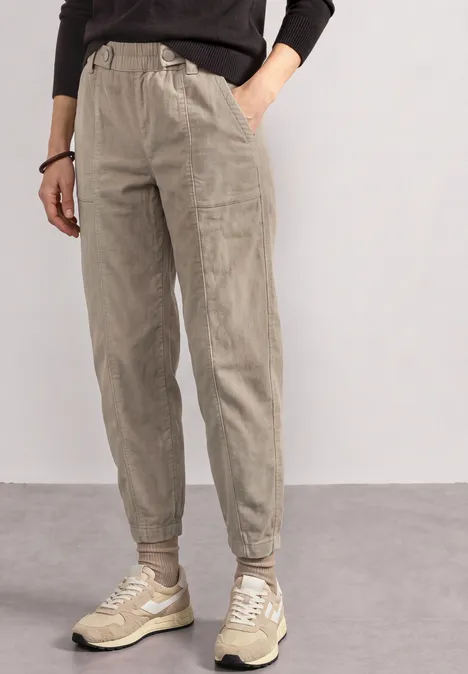 model trägt beige, lässige Jogginghose mit Bündchen und Kordelzug, dazu Sneakers.