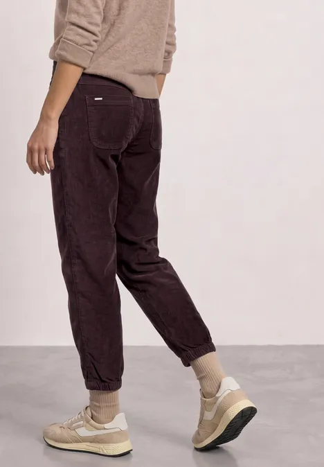 Person steht seitlich, trägt braune Cordhose und beige Sneaker.