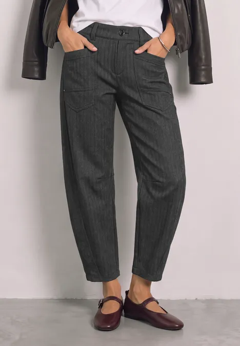 Damen in grauen Nadelstreifen-Hosen, weißem Shirt und dunkelroten Mary-Jane-Schuhen.