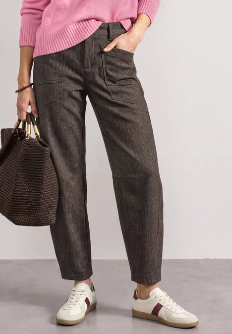 Vrouw in bruin fijngestreepte broek, witte sneakers en met een grote handtas.