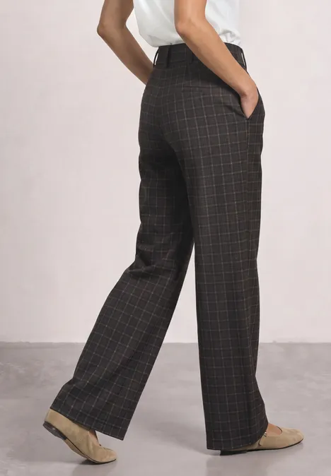 Iemand draagt een wijd, bruin geruit broek met zakken en beige loafers.