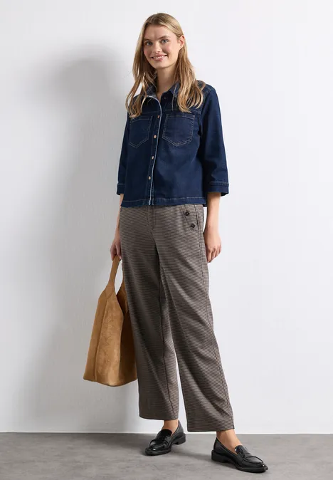 High Waist Straight Leg Hose mit Knopfdetails sanded amber Frau mit dunkelblauer Jeans-Bluse, grauer Hose, schwarzen Loafers und einer braunen Tasche vor weißer Wand.