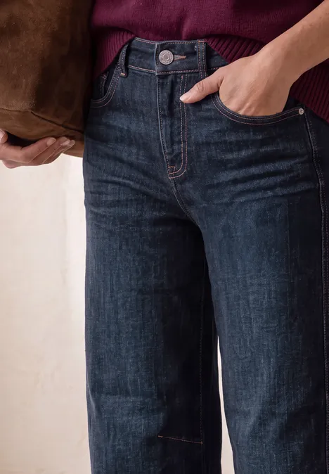 High Waist Barrel Leg Jeans im Loose Fit Dark Blue Washed Nahaufnahme einer Person in weiten, hochgeschnittenen dunkelblauen Jeans, Hand in der Tasche und brauner Schultertasche