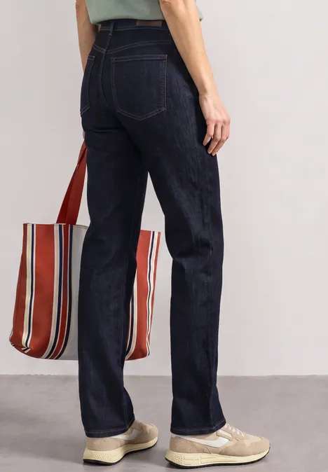 Person von hinten in dunkelblauen Jeans, beigefarbenen Sneakern und gestreifter Stofftasche.
