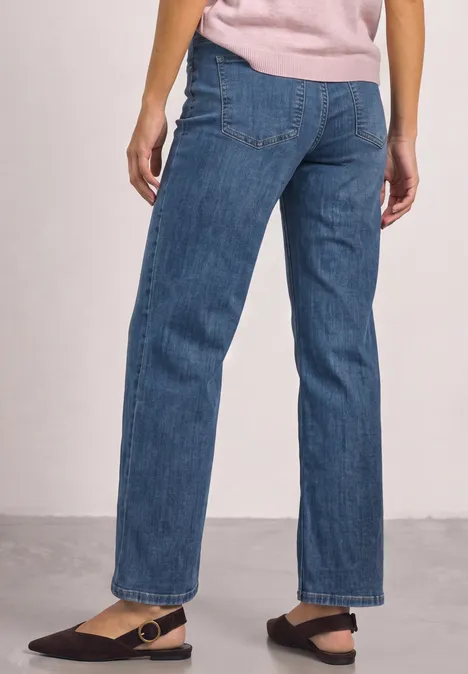 Mid Waist Straight Leg Jeans im Casual Fit Mid Blue Washed Frau trägt gerade geschnittene blaue Jeans und schwarze Riemchensandalen.