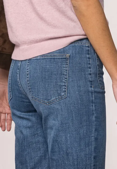 Mid Waist Straight Leg Jeans im Casual Fit Mid Blue Washed Person von hinten, trägt blaue Jeans und rosa Oberteil.