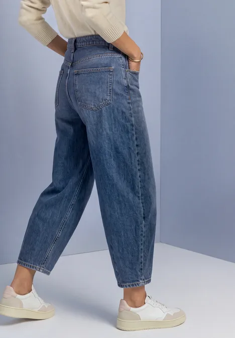 Jean taille haute à Barrel Leg, coupe ample Medium Blue Soft Washed Silhouette de profil portant un jean bleu ample taille haute et des baskets blanches, mains en poches.
