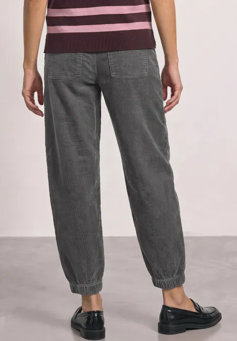 High Waist Barrel Leg Hose mit Elastikbund eclipse grey Eine Person von hinten in dunkelgrauen, elastischen Stoffhosen mit Bündchen und schwarzen Slippern.