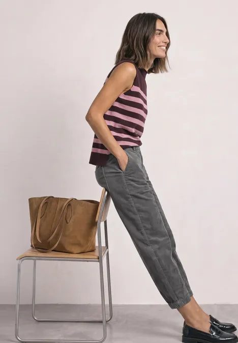 High Waist Barrel Leg Hose mit Elastikbund eclipse grey Frau in ärmellosem Ringelshirt lehnt lässig an Stuhl, graue Hose, schwarze Schuhe, braune Tasche am Stuhl