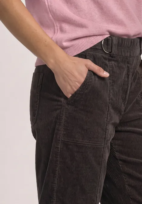 Person trägt eine braune Cordhose mit Hand in der Tasche und ein rosafarbenes Oberteil.