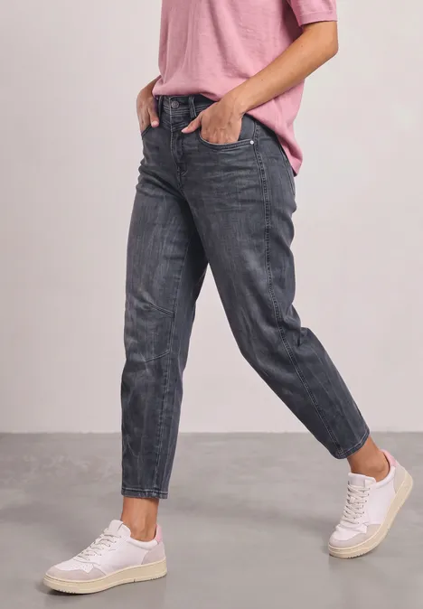 High Waist Barrel Leg Jeans im Loose Fit Steel Grey Wash Person in taillierten dunkelgrauen Jeans, weißen Sneakern und rosa Shirt vor neutralem Hintergrund.