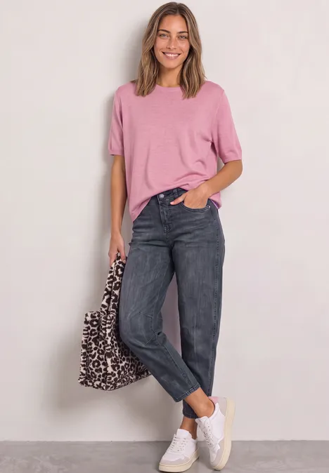 High Waist Barrel Leg Jeans im Loose Fit Steel Grey Wash Frau in rosa Shirt, schwarzen Jeans und weißen Sneakern mit Leoparden-Tasche.