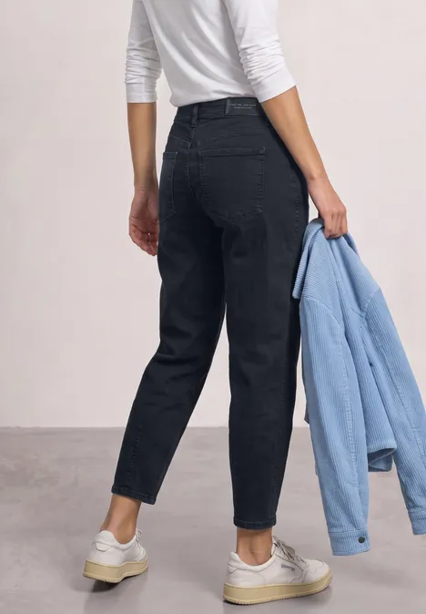 High Waist Barrel Leg Jeans im Loose Fit blue black soft wash Rückansicht einer Person in schwarzen Jeans, weißem Shirt und weißen Sneakern, die eine hellblaue Jacke hält.