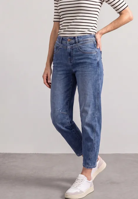Frau in blauen Jeans, gestreiftem Shirt und weißen Sneakern.