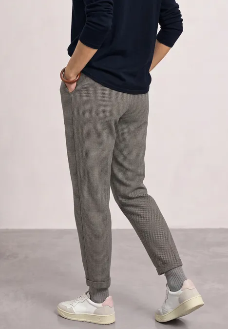 High Waist Barrel Leg Hose im Casual Fit Black Mann von hinten in grauen Stoffhosen und weißen Sneakern vor neutralem Hintergrund.