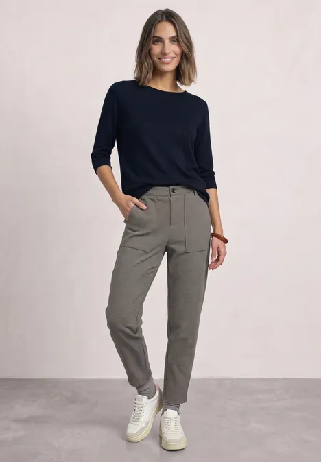 High Waist Barrel Leg Hose im Casual Fit Black Eine Frau in dunkelblauem Pullover, khakifarbenen Hosen und weißen Sneakern lächelt entspannt