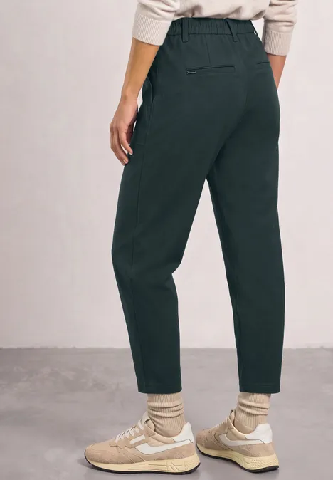 Dunkelgrüne, hoch taillierte, gerade geschnittene Hose, kombiniert mit hellen Sneakers und Socken