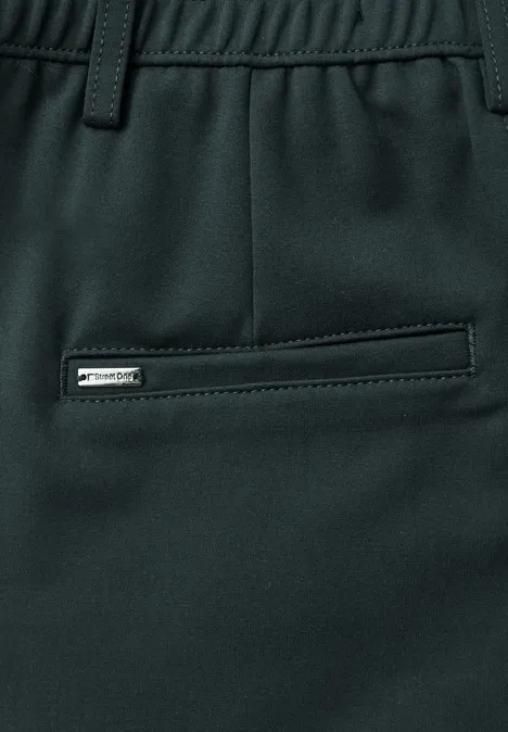 Close-up einer dunkelgrünen Hose mit elastischem Bund, Gürtelschlaufen und seitlicher Reißverschlusstasche.
