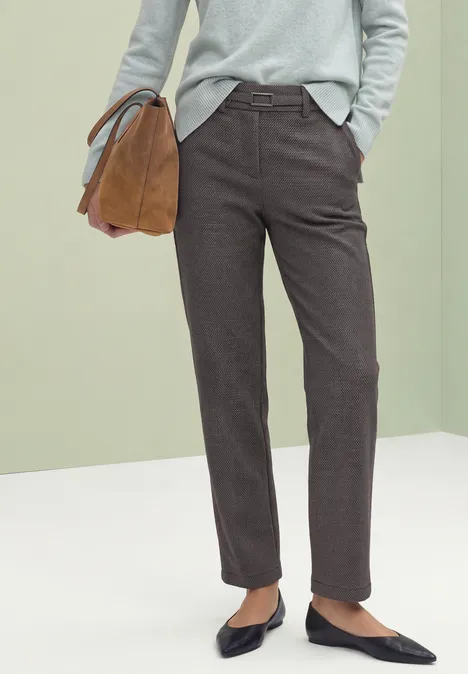 Personne vêtue d’un pull gris, pantalon marron foncé, ballerines noires, tenant un sac camel.