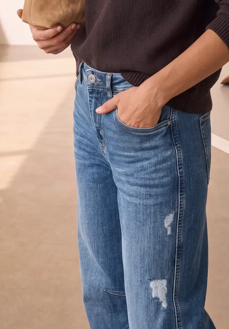 Eine Person in blauen Jeans steckt die Hand in die Hose, Oberkörper teils sichtbar.